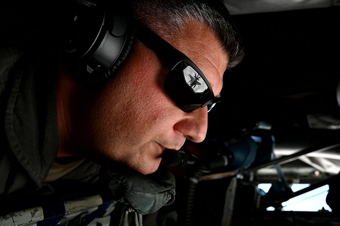 An airman wearing sunglasses in the cockpit of an aircraft focuses on an aerial refueling.
