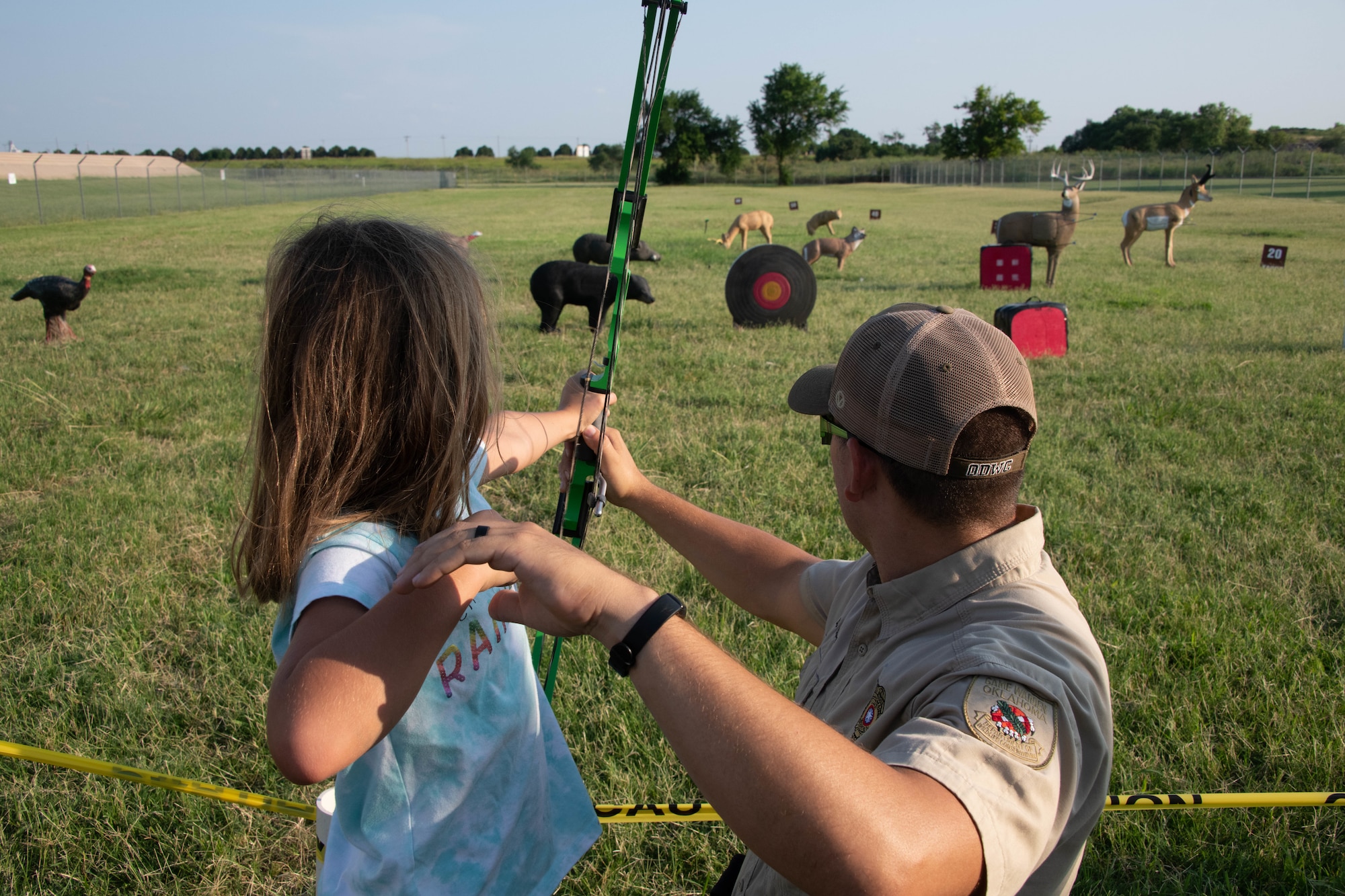 Daniel Perkins, Oklahoma Department of Wildlife Conservation state game warden helps Genevieve Allen, daughter of U.S. Air Force Master Sgt. Nathan Allen, 97th Air Mobility Wing public affairs superintendent, shoot her bow on Altus Air Force Base, Oklahoma, July 30th, 2021. Outdoor recreation supports family and individual well being, unit cohesion, and fitness through many programs and facilities on base. (U.S. Air Force photo by Airman 1st Class Trenton Jancze)