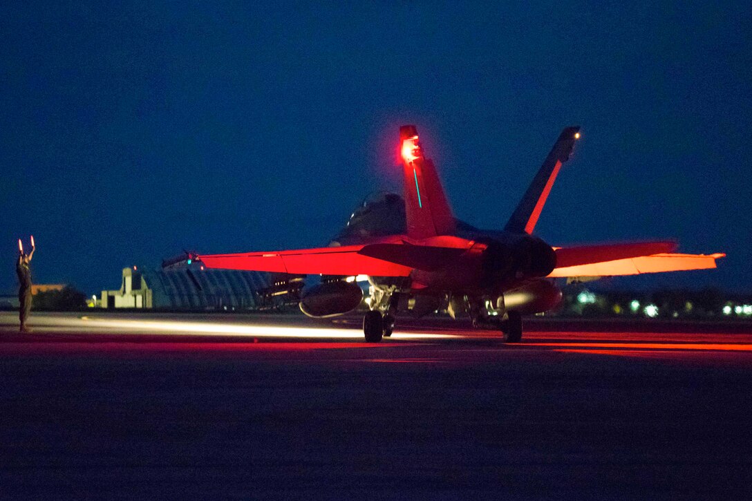 A Marine signals to aircraft on a tarmac illuminated by a red light.