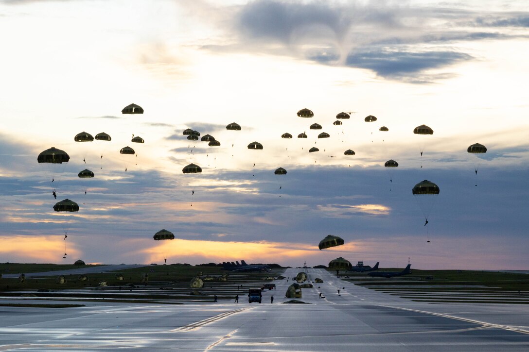 Pratroopers descend against a partly cloudy orange sky.