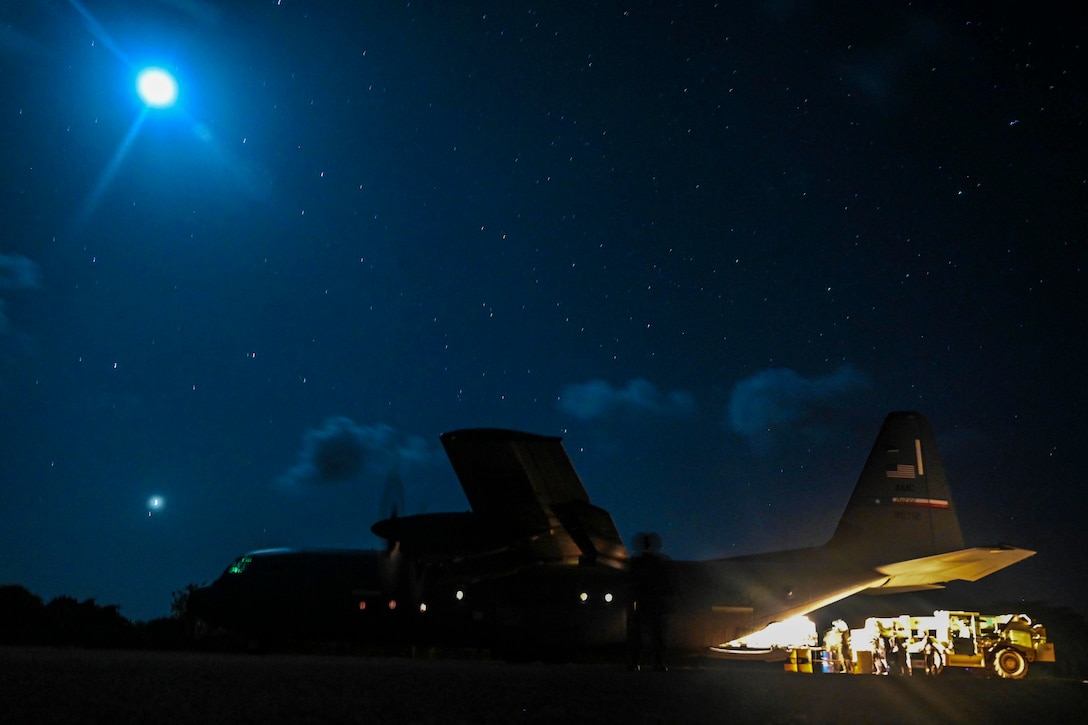 Airmen load equipment into an aircraft at night.