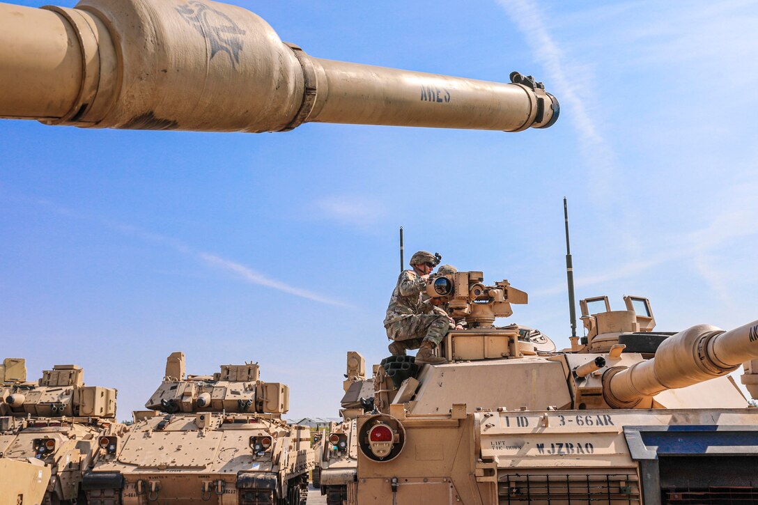 A soldier kneels on top of a tank.