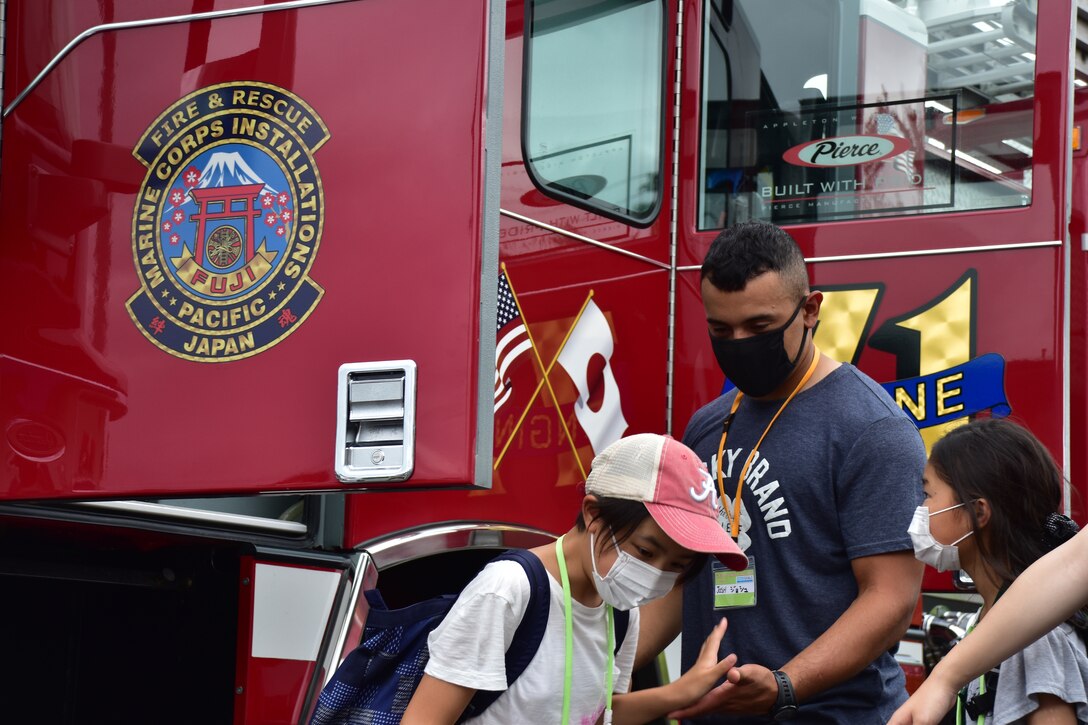 Lance Cpl. Joshua Dejesus, Combined Arms Training Center Camp Fuji motor transportation operator, helps local children explore the inside of a fire truck during a tour of Combined Arms Training Center Camp Fuji’s fire department, Aug. 7, 2021, Shizuoka, Japan. Marines and Sailors from the installation volunteered with the camp and provided children the opportunity to speak with native English speakers. Dejesus is a native of Paterson, New Jersey. (U.S. Marine Corps photo by Katie Gray)