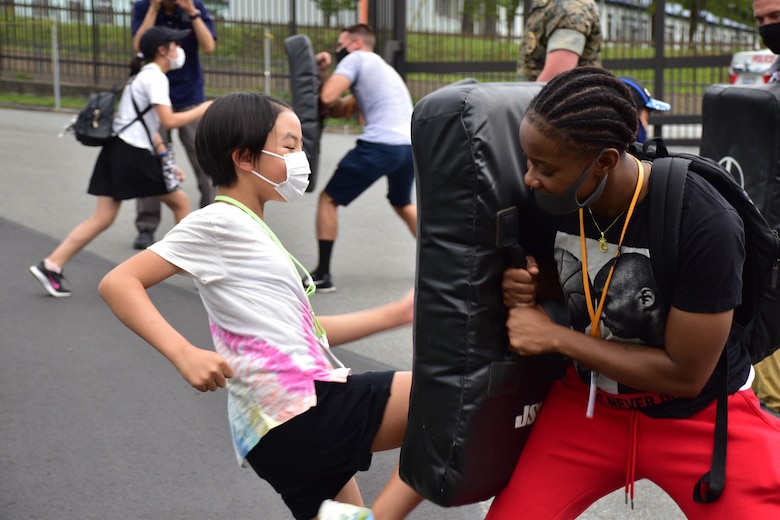 A local Japanese child practices kicking a training pad held by Sgt. Takiyah Wesley, Combined Arms Training Center Camp Fuji supply sergeant, Aug. 7, 2021, Shizuoka, Japan. Marines and Sailors from the installation volunteered at the National Chuo Youth Friendship Center’s fifth annual English camp, where they engaged local children in conversation and activities. Wesley is a native of Memphis, Tennessee. (U.S. Marine Corps photo by Katie Gray)