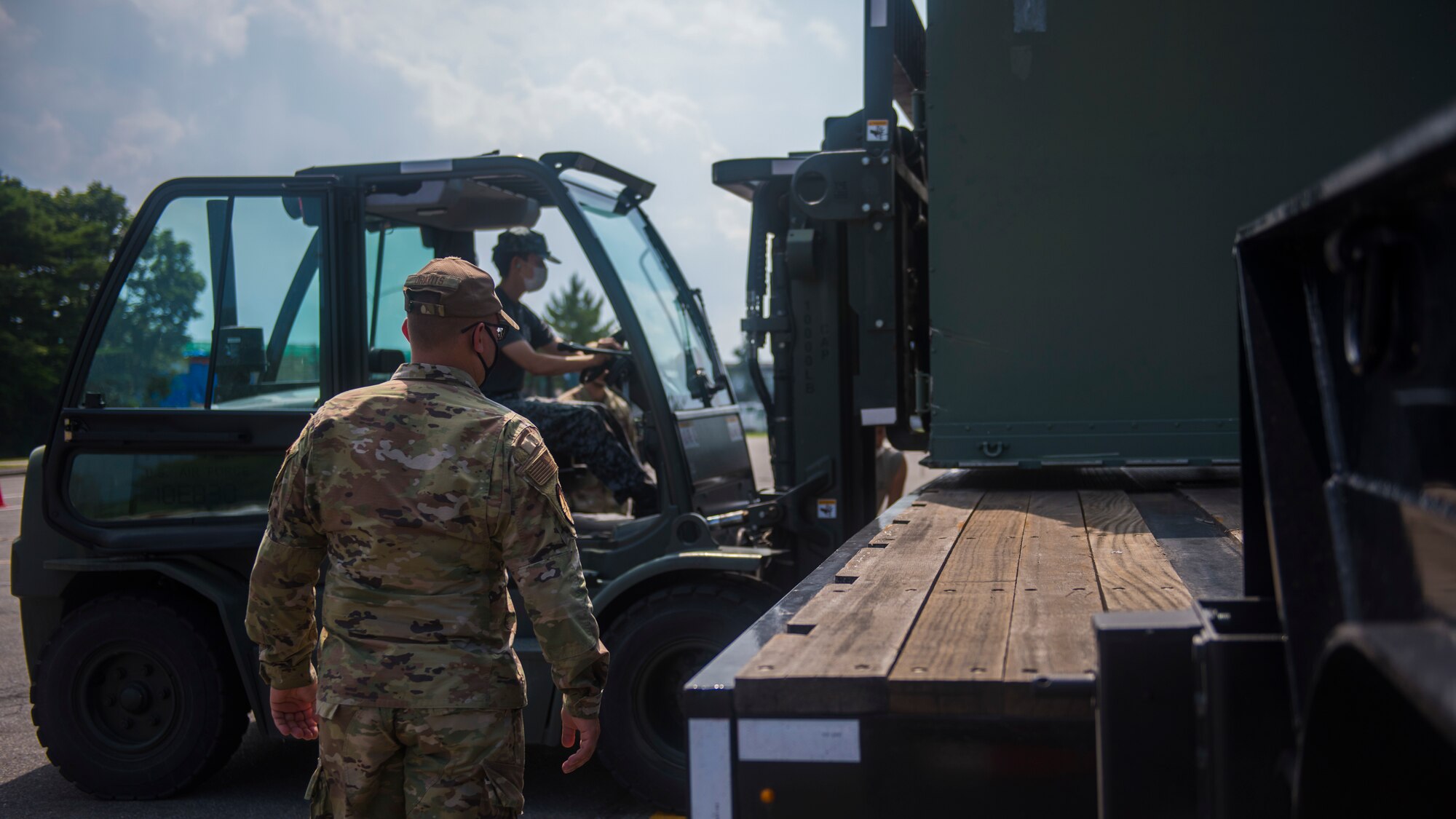 USAF member watches as JASDF members operate a forklift to place cargo on a truck.