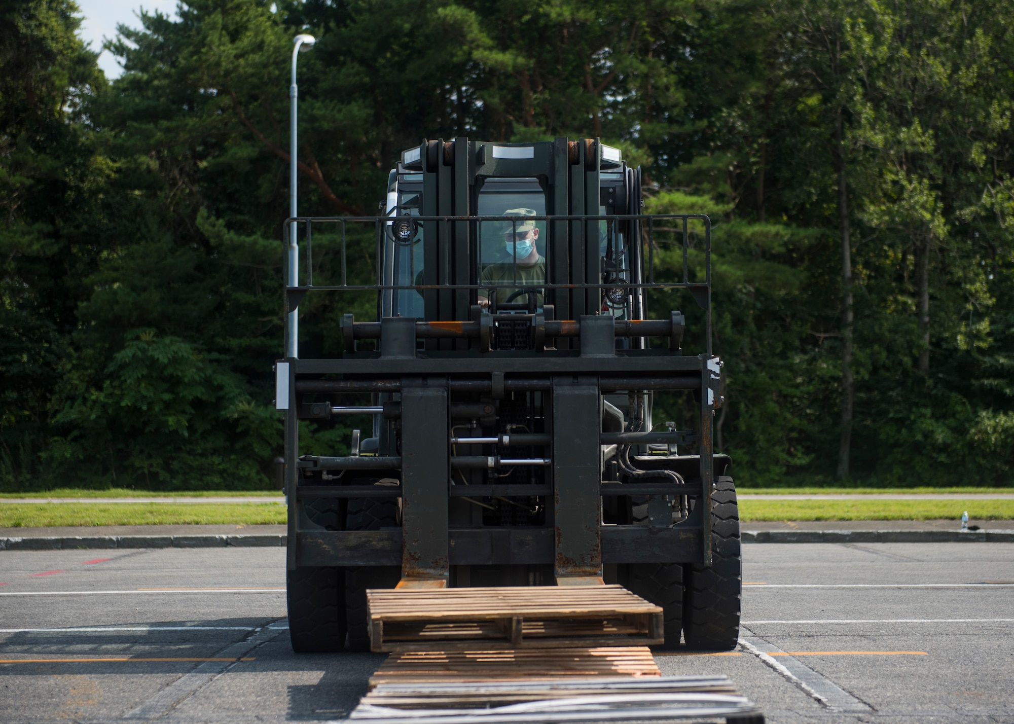 USAF member operates a forklift to pick up wooden pallets off of the ground.