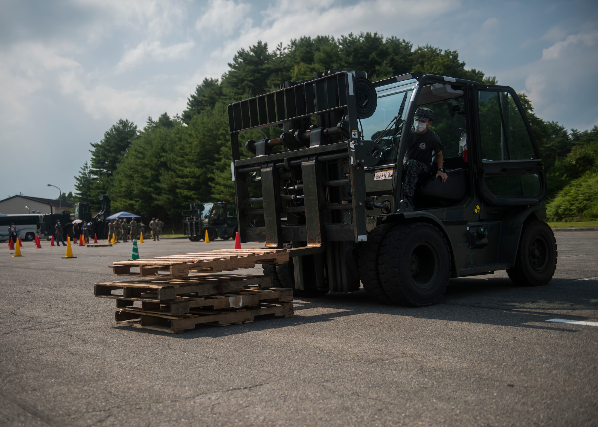 JASDF member operates a forklift to stack wooden pallets on the ground.