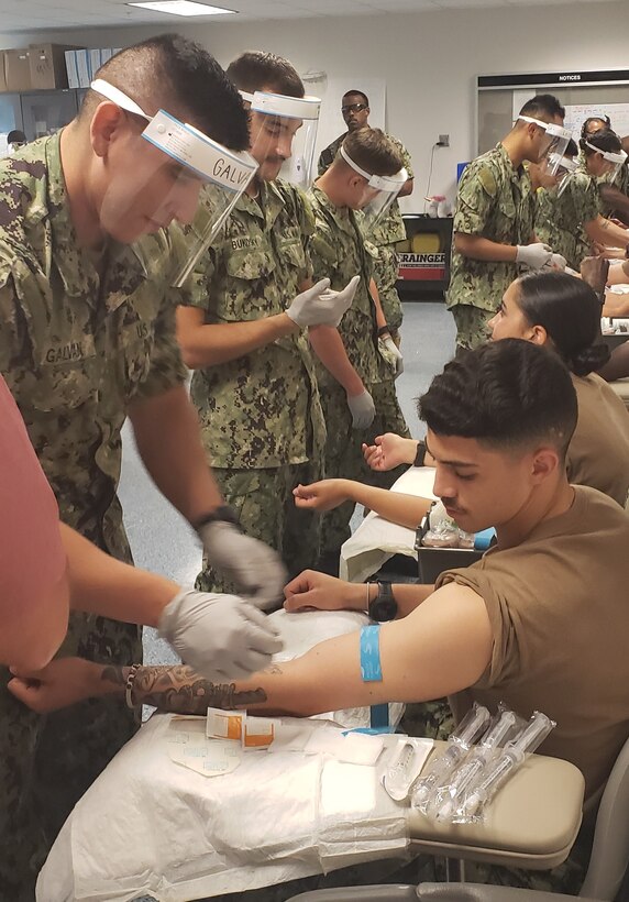 Students in the Navy Hospital Corpsman Basic program at the Medical Education and Training Campus practice performing a venipuncture procedure on each other.