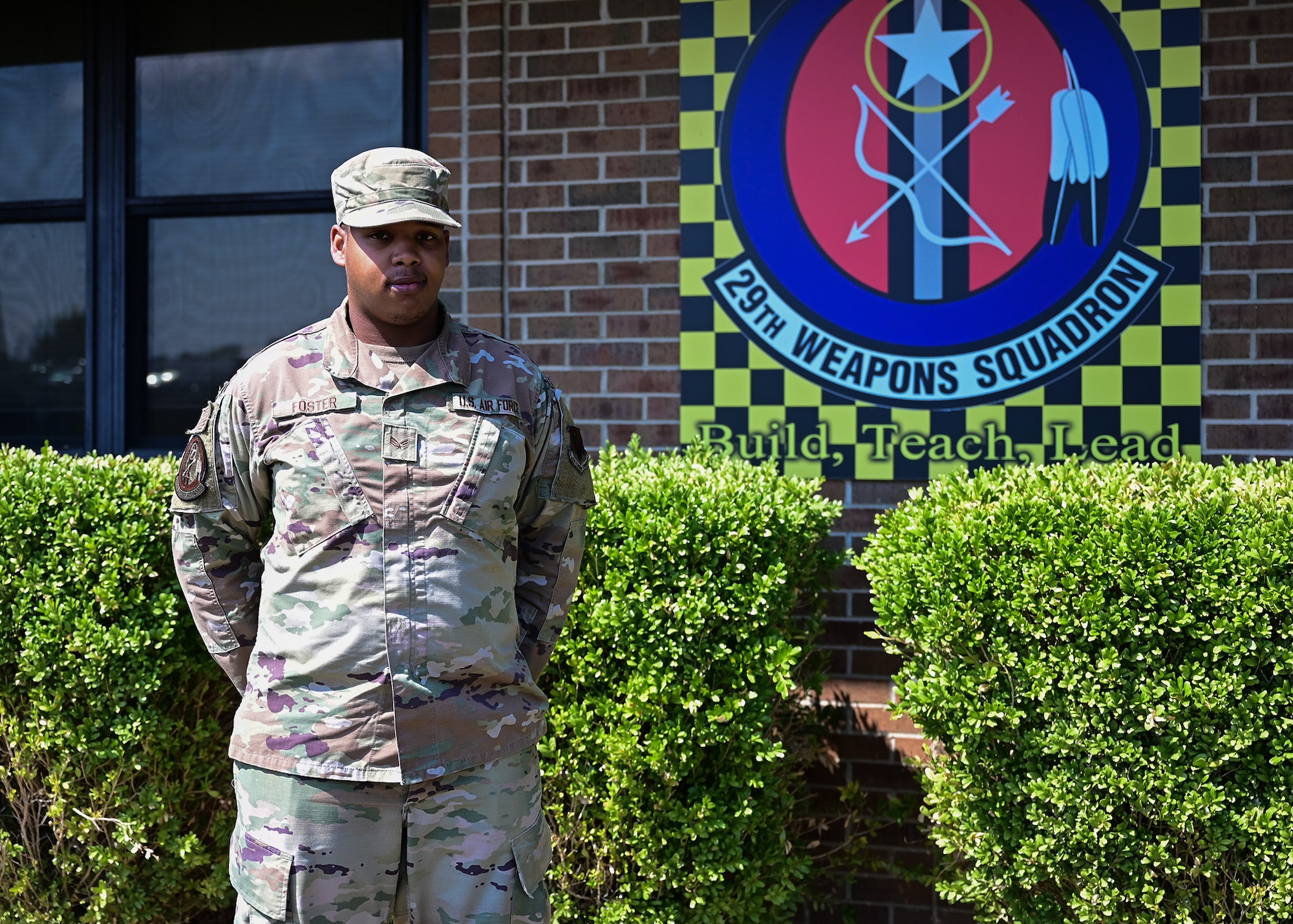 An Airman stands in front of a sign that displays the 29th Weapons Squadron patch.