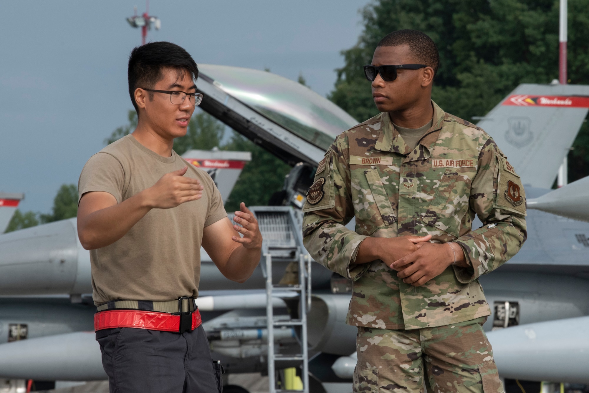 U.S. Air Force Senior Airman Peter Ho, 480th Expeditionary Fighter Squadron crew chief, (left) explains how to marshall a U.S. Air Force F-16 Fighting Falcon with U.S. Air Force Airman First Class Tyquan Brown 480th EFS Security Forces armorer at Łask Air Base, Poland, August 4, 2021. The Airmen participated in a training program that allows Airmen to shadow a dedicated crew chief during the launch process of an F-16 Fighting Falcon. (U.S. Air Force photo by Tech. Sgt. Anthony Plyler)