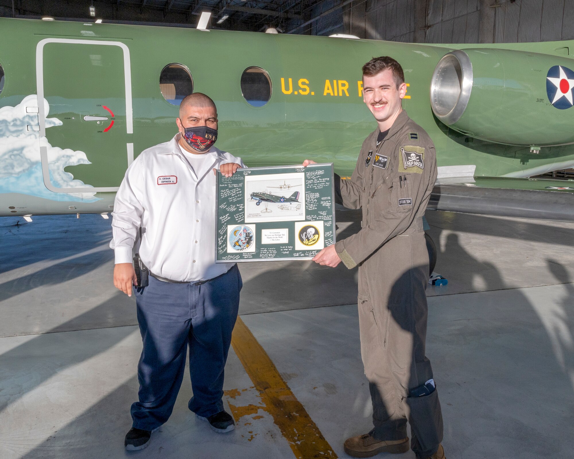Cesar Espinoza, Laughlin Air Force Base corrosion shop supervisor, poses with U.S. Air Force Capt. Marc Howe, 86th Flying Training Squadron flight commander, while holding a plaque presented to Laughlin maintainers for their work with the heritage tail on August 13, 2021. The paint scheme of the aircraft reflects a heritage that dates back to the Douglas B-18 “Bolo” of World War II.(U.S. Air Force Photo by Senior Airman Nicholas Larsen)
