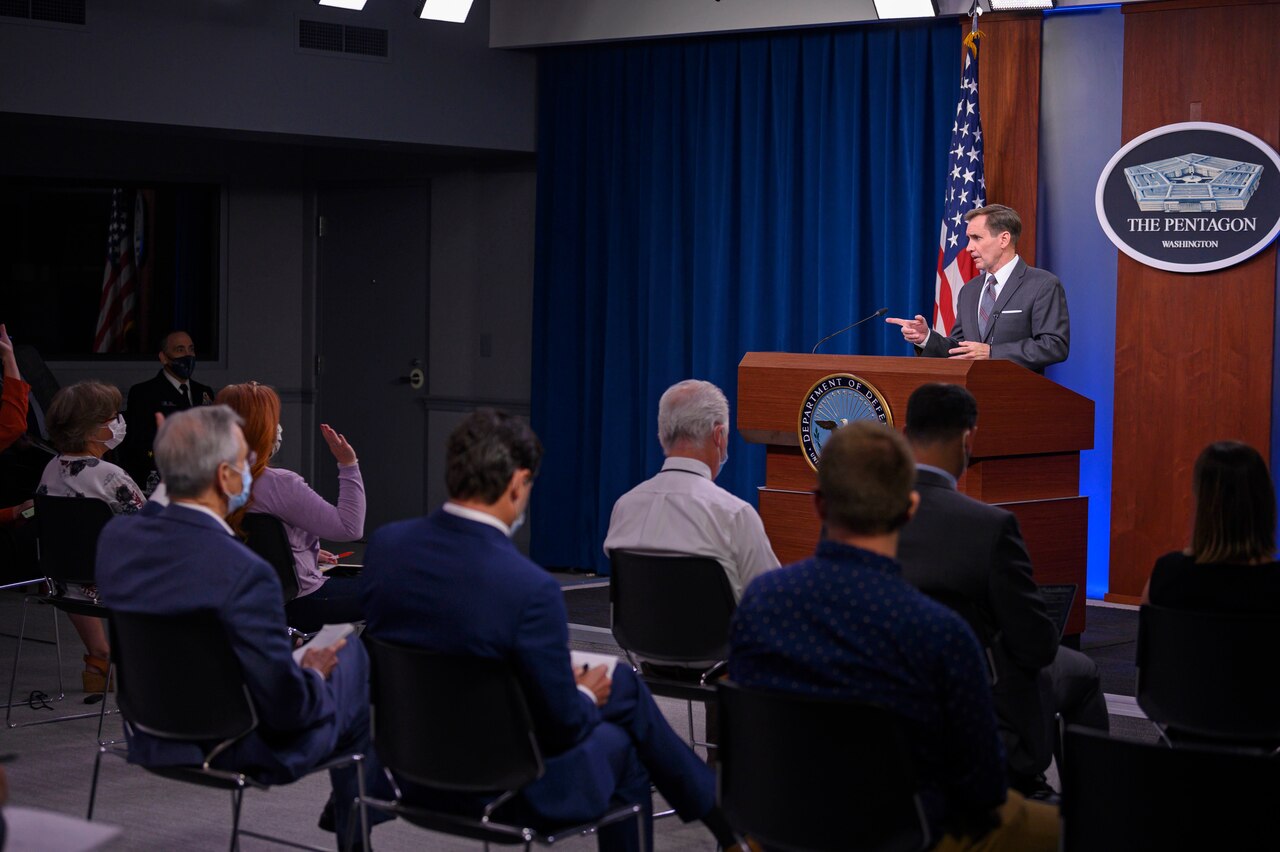 Pentagon Press Secretary John F. Kirby stands at a podium and speaks to a group of people.
