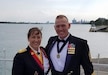 Two Soldiers stand next to each other smiling in their dress mess uniforms with a lake behind them.
