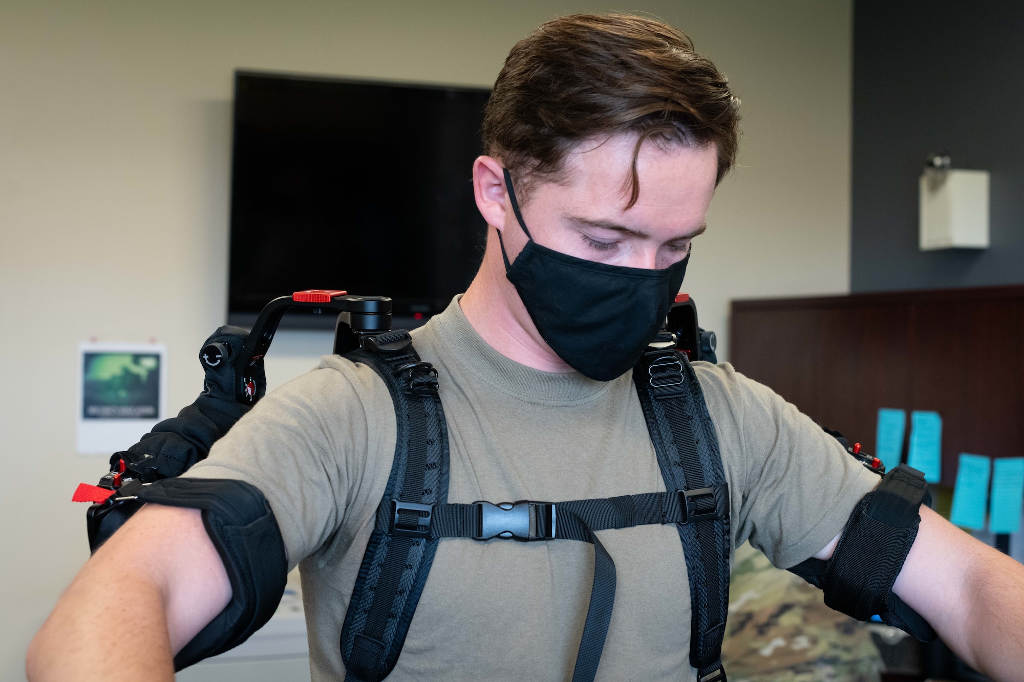 Airman stands with suit strapped around shoulders and arms.