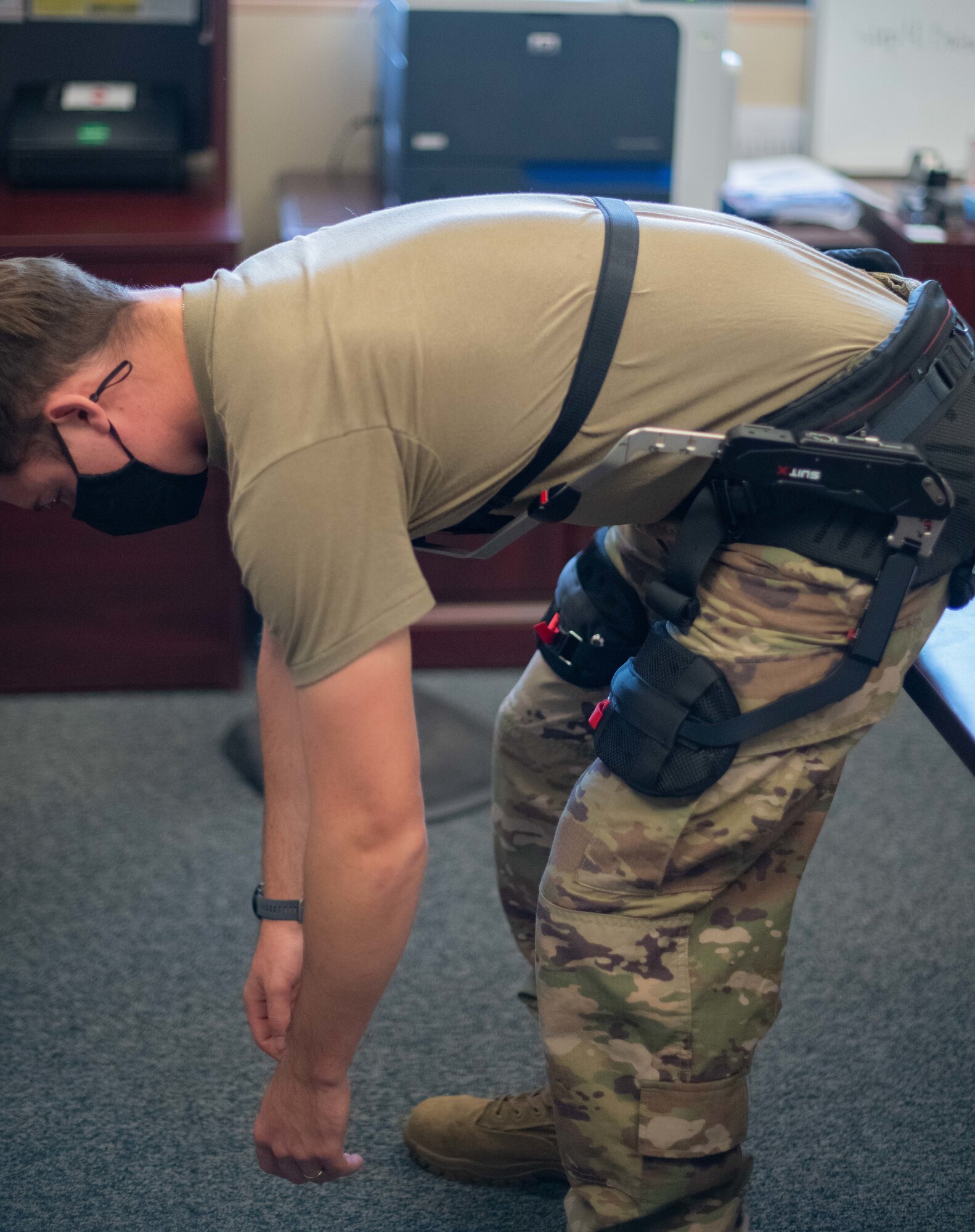 An Airman strikes a bent-over pose with a suit attached to his chest, lower back, hips and thighs.