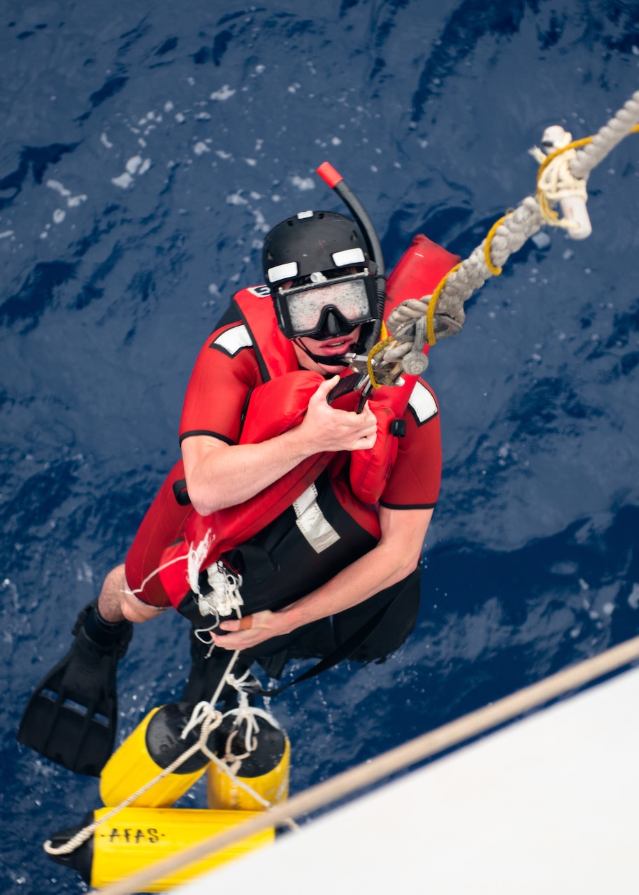 Coast Guard Seaman Jaiden Hartley is hoisted back onto the Coast Guard Cutter Munro after completing a man overboard drill in the Pacific Ocean, July 28, 2021. The Munro and its crew are currently deployed to the Western Pacific, patrolling and conducting operations while strengthening partnerships with allies in the region.