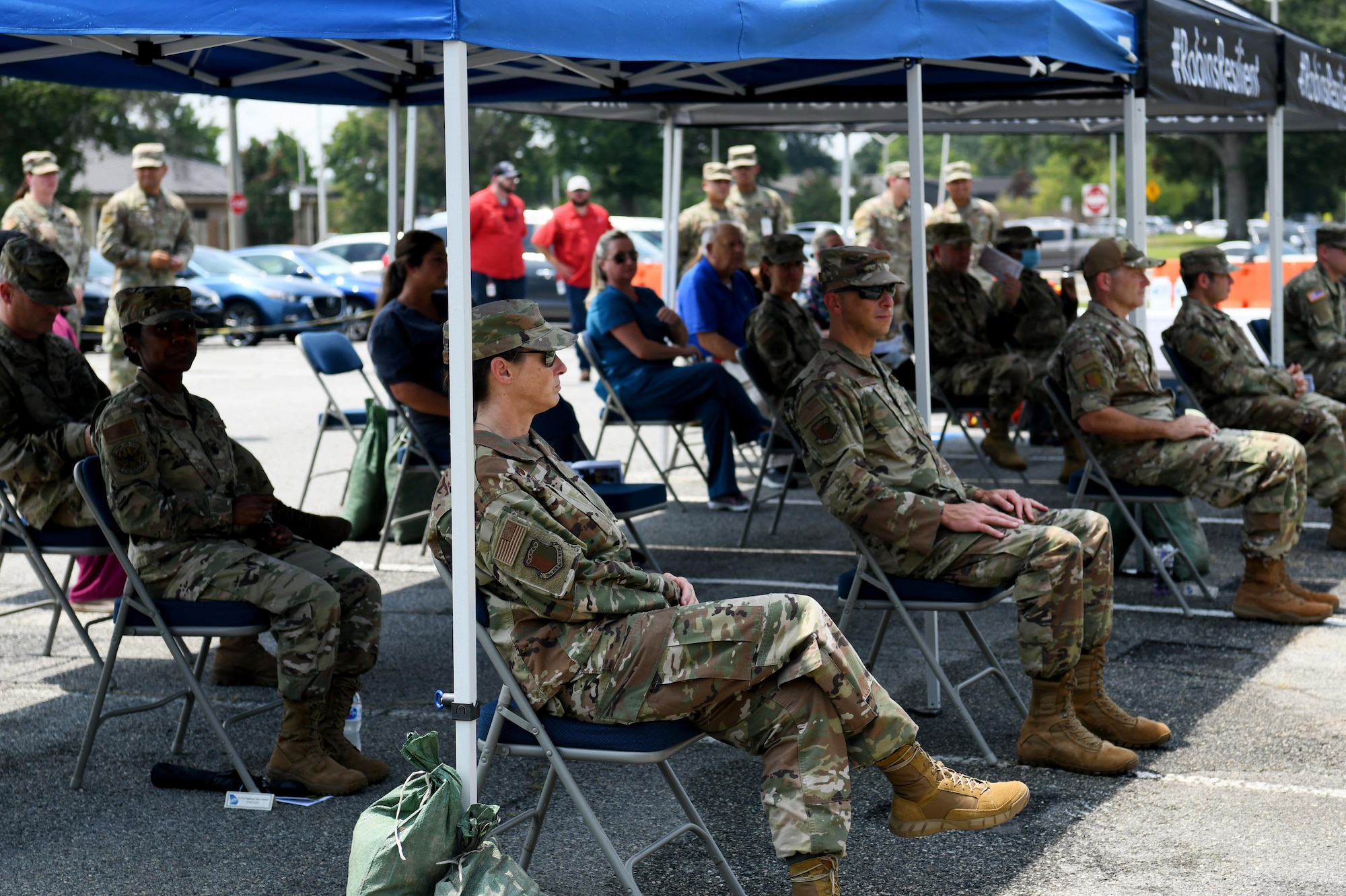 Photo shows group of people sitting under canopies.