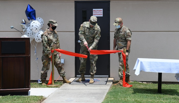 Photo shows three people cutting a red ribbon in front of the facility.