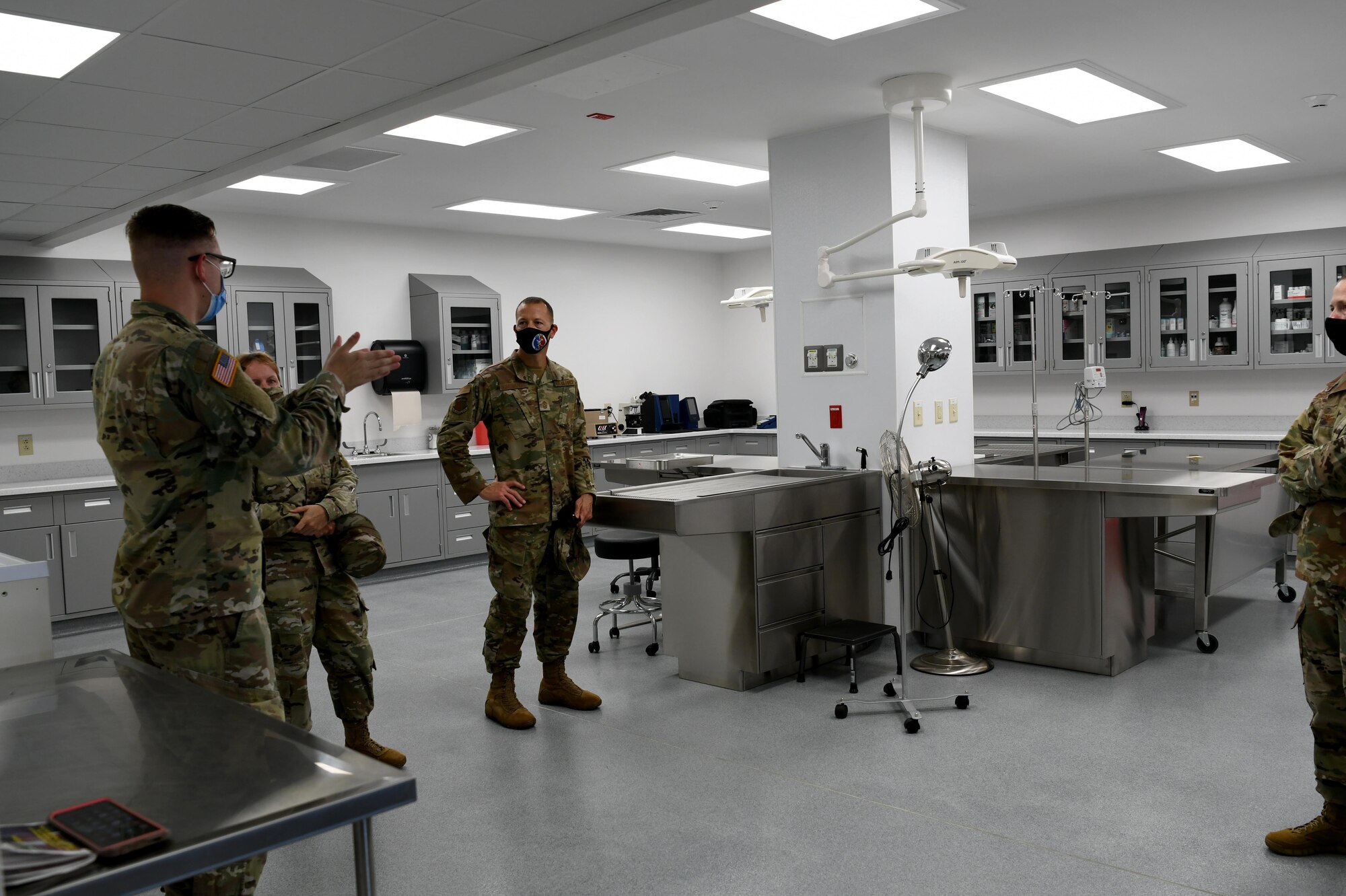 Photo shows male Airmen speaking to a group of people inside a medical examination room.