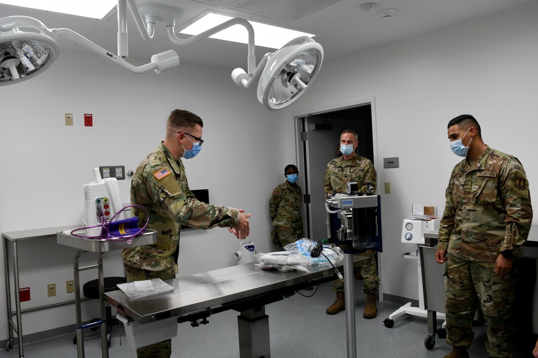 Photo shows a male Airmen pointing at medical equipment speaking to a group of people.