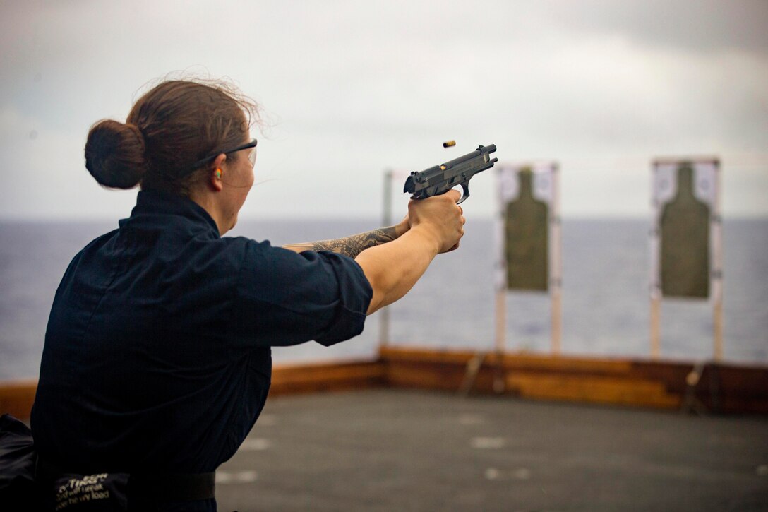 A sailor fires at a target aboard a ship.