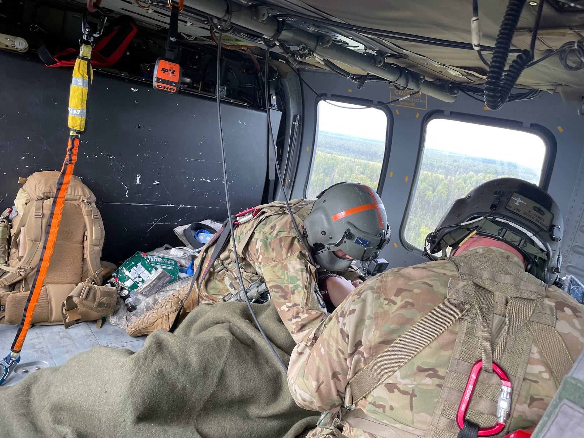 Staff Sergeant Damion Minchaca (left), an Alaska Army National Guard flight paramedic, provides critical en route care to a 75-year old man after he fell into a river and drowned, requiring immediate resuscitation, and sustaining multiple injuries, Aug. 12, 2021. Spec. Stefano James (right), a UH-60L Black Hawk medevac helicopter crew chief, provided medical assistance. The aircraft and crew, from Detachment 2, G Company, 2nd Battalion, 211th Aviation Regiment, hoisted the patient into the aircraft and provided medevac support. A fishing guide saved the patient’s life, and the seamless, joint effort of the Alaska Air National Guard’s Rescue Coordination Center and Army National Guard’s Det. 2, G-Co, 2-211th AVN ensured a successful rescue and crucial medical care during transport to Providence Alaska Medical Center in Anchorage. The patient was delivered to the hospital within two hours of the AST request for support, and he was passed directly to a physician on site for continuation of necessary medical care. (Courtesy photo by U.S. Army National Guard crew chief, Staff Sgt. Bradley McKenzie)
