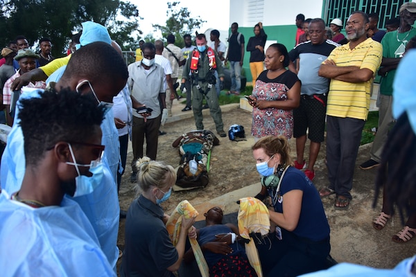 People stand around doctors attending a man lying on a mat.