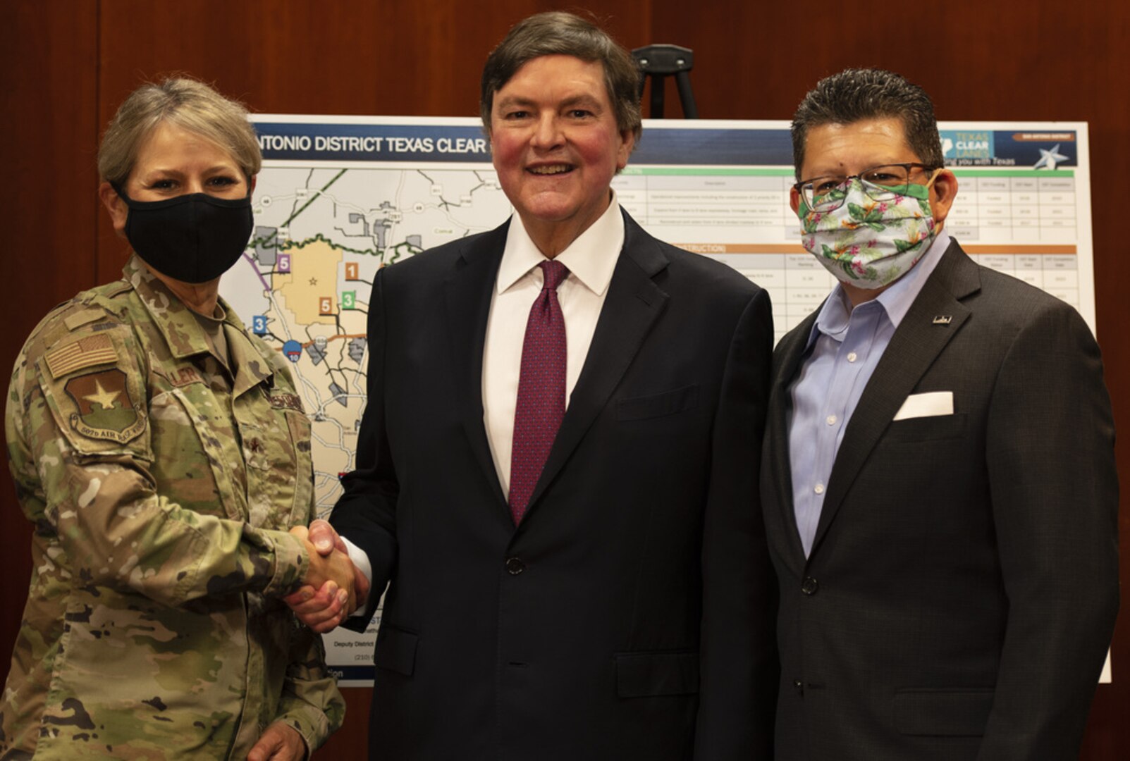 A woman and two men pose for a photo after a press conference.