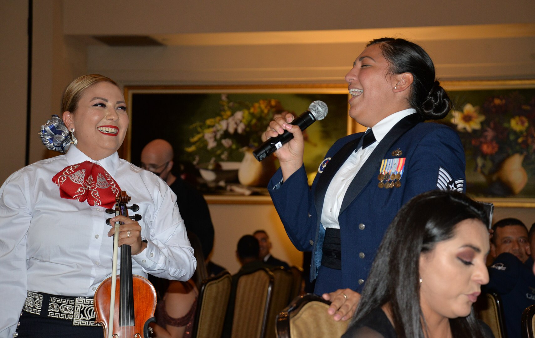 Tech Sgt. holds mike and sings while mariachi group member smiles.