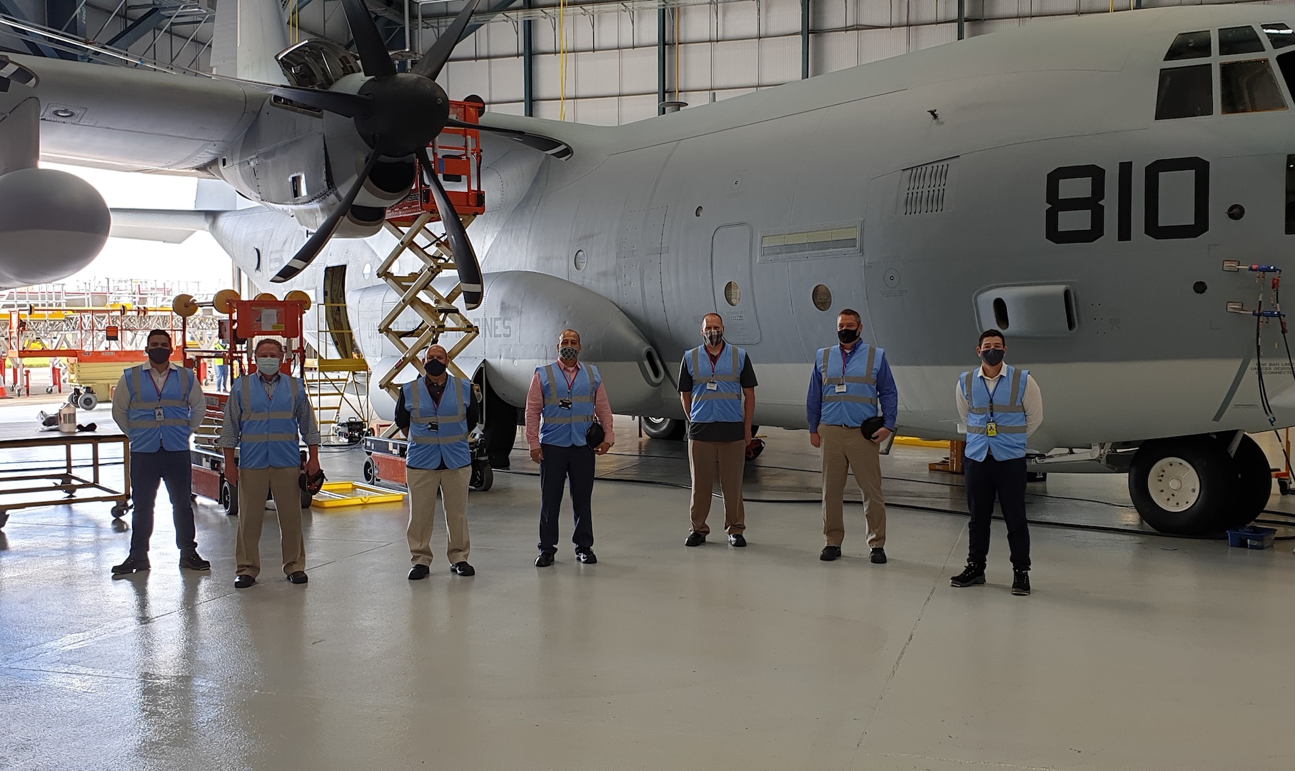 Seven personnel pose in front of an aircraft inside a hangar.