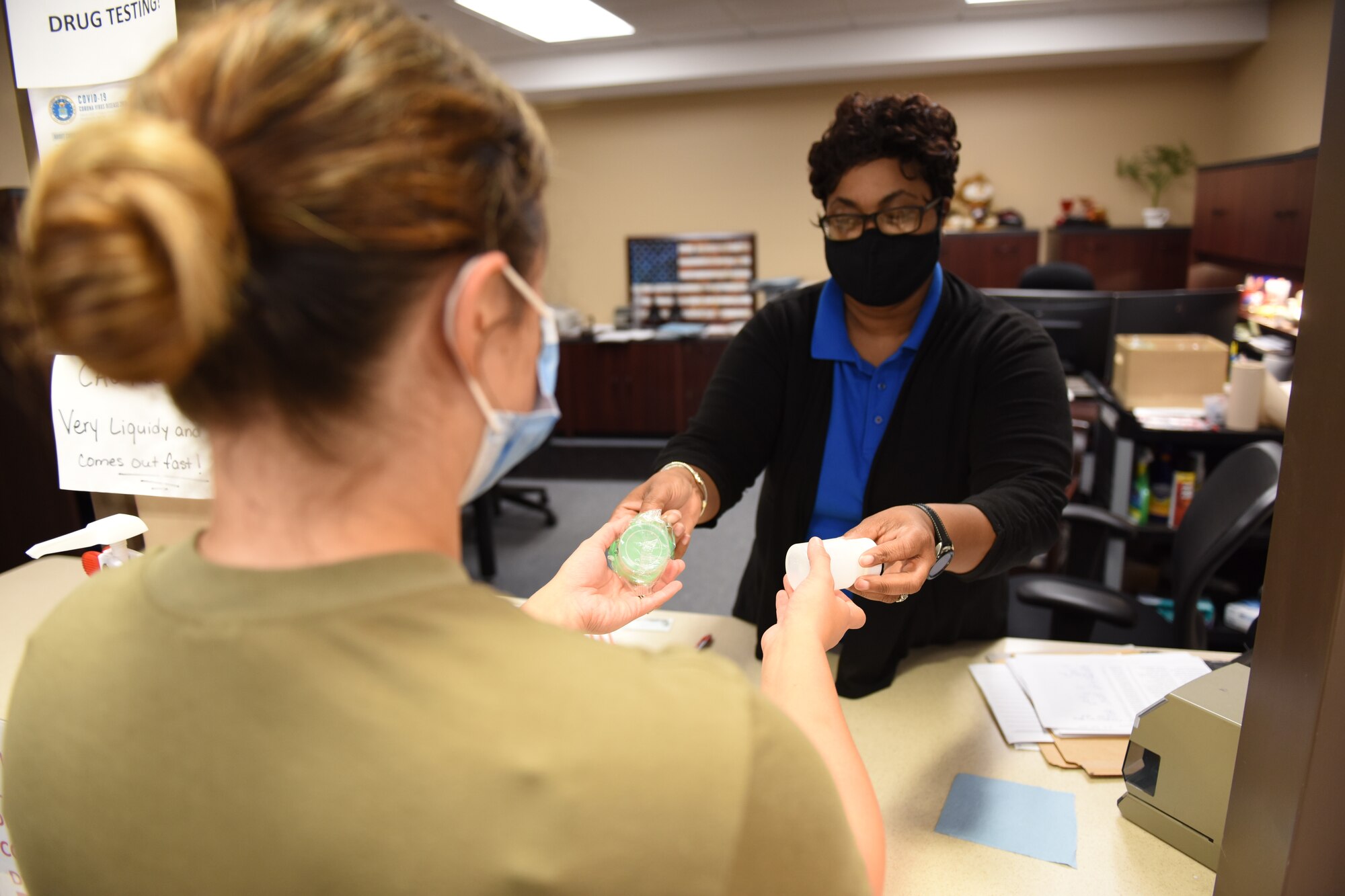 Photo shows a woman handing sample cups to an Airman.