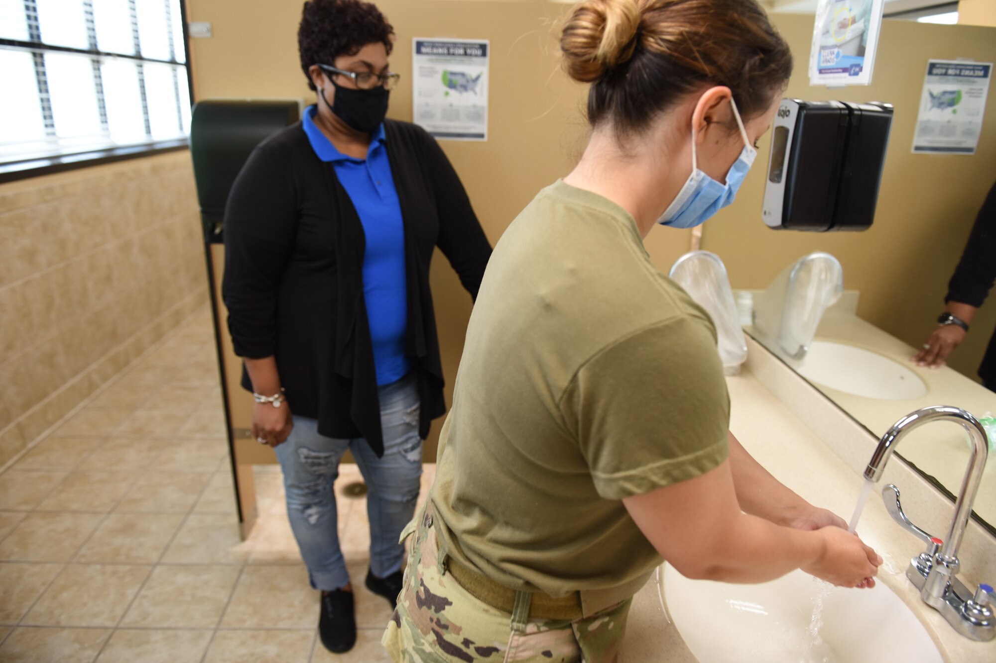 Photo shows Airman washing her hands while another woman watches.