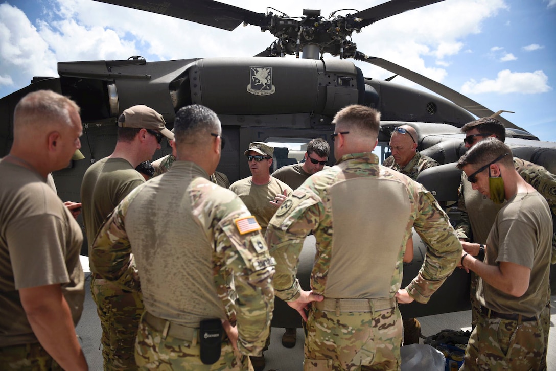 Soldiers stand and talk in front of a parked helicopter.