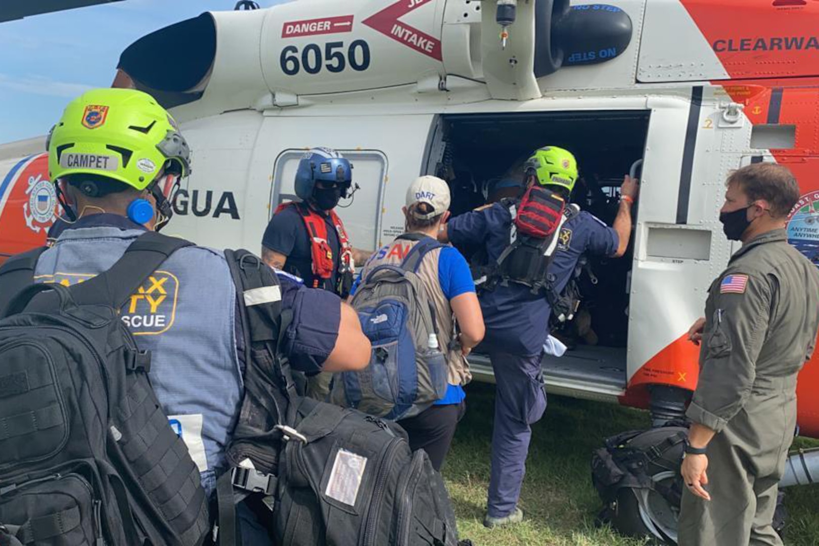 Five people loaded with gear climb into a helicopter.