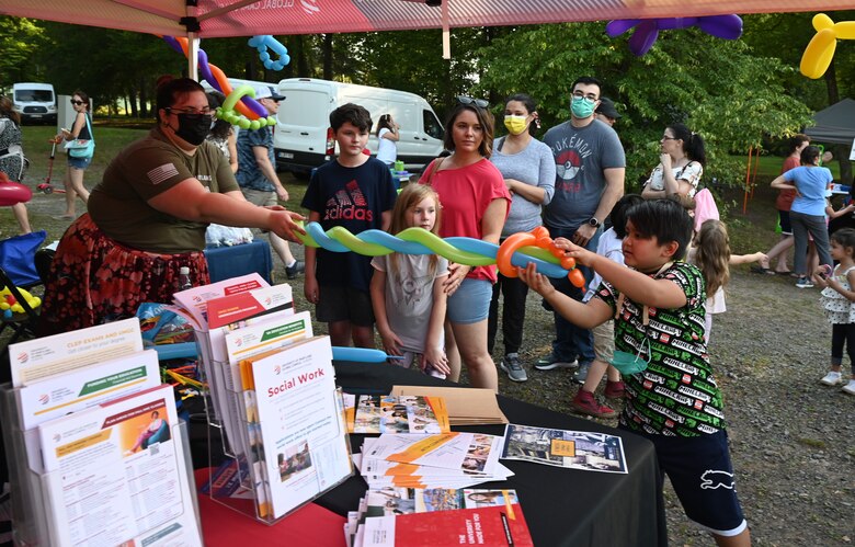 A volunteer hands a balloon to a child at the Community Cares Partners Party in the Park event at the Vogelweh Military Complex, Germany, Aug. 12, 2021. The 86th Force Support Squadron hosted the Party in the Park to bring people together to enjoy food and music while learning about community resources provided by the 86th Force Support Squadron Airman and Family Readiness Center. (U.S. Air Force photo by Senior Airman Thomas Karol)