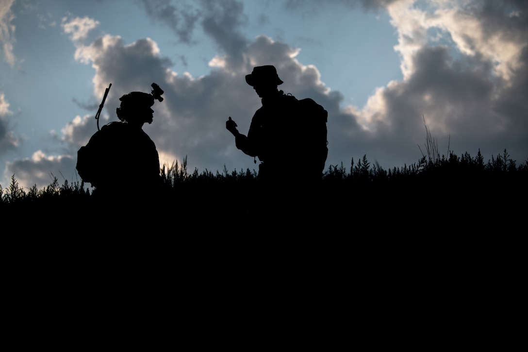 Two airmen are silhouetted as they stand together in a large field.