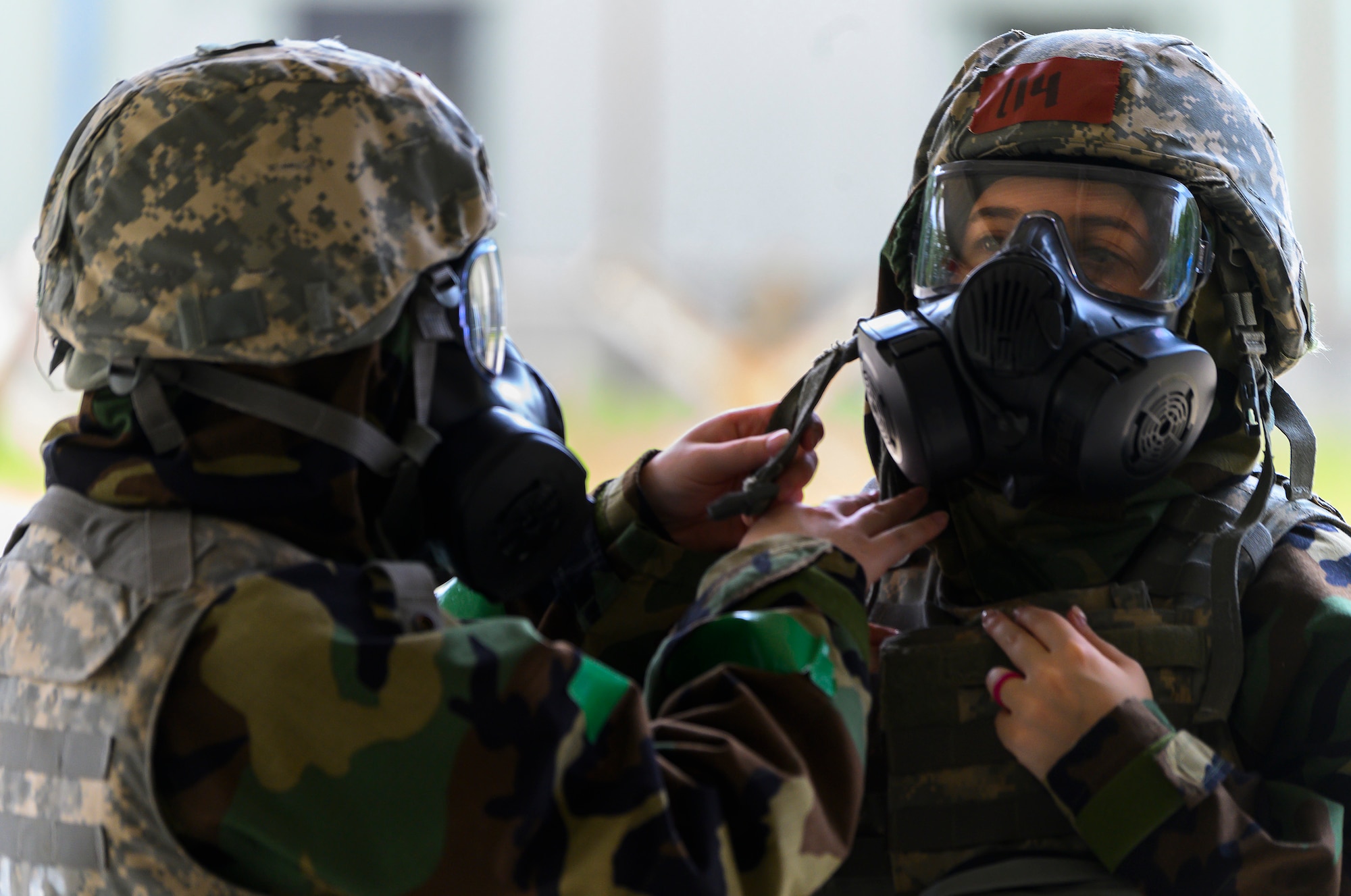 An Airman with the 88th Air Base Wing helps another with the donning of a M50 gas mask during training Aug. 11. 2021 at Wright-Patterson Air Force Base, Ohio. Periodic refresher training helps Airmen prepare for emergencies. (U.S. Air Force photo by R.J. Oriez)