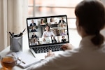 woman looks at a laptop screen display showing 14 other individuals in a virtual meeting