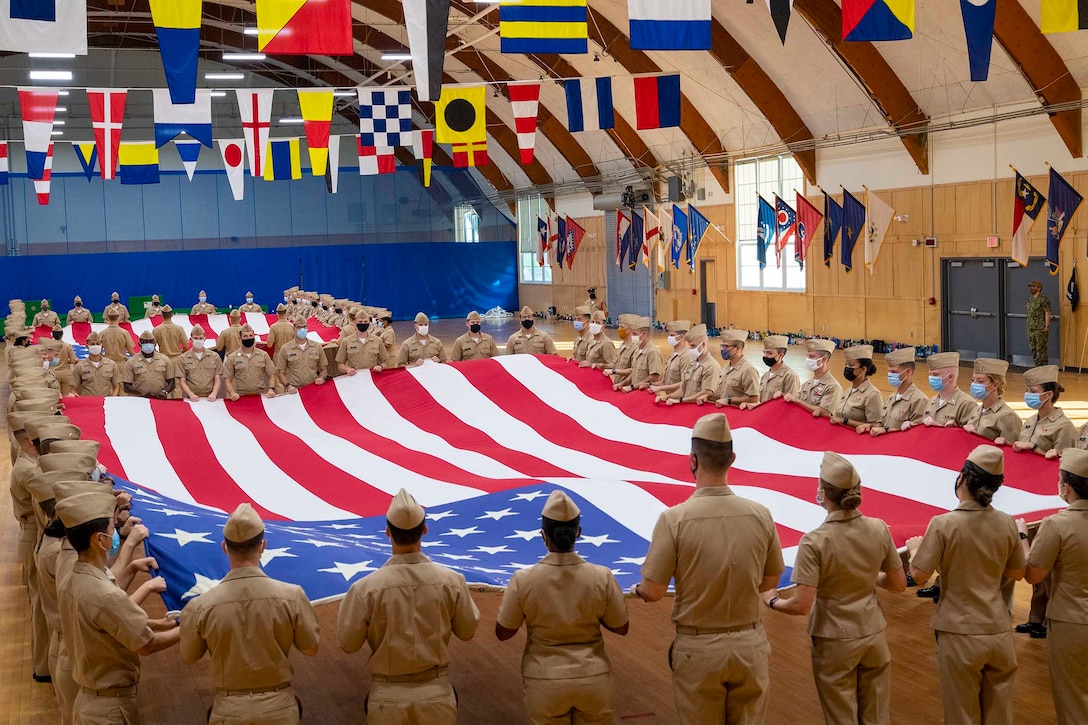 A large group of sailors carry two large American flags.