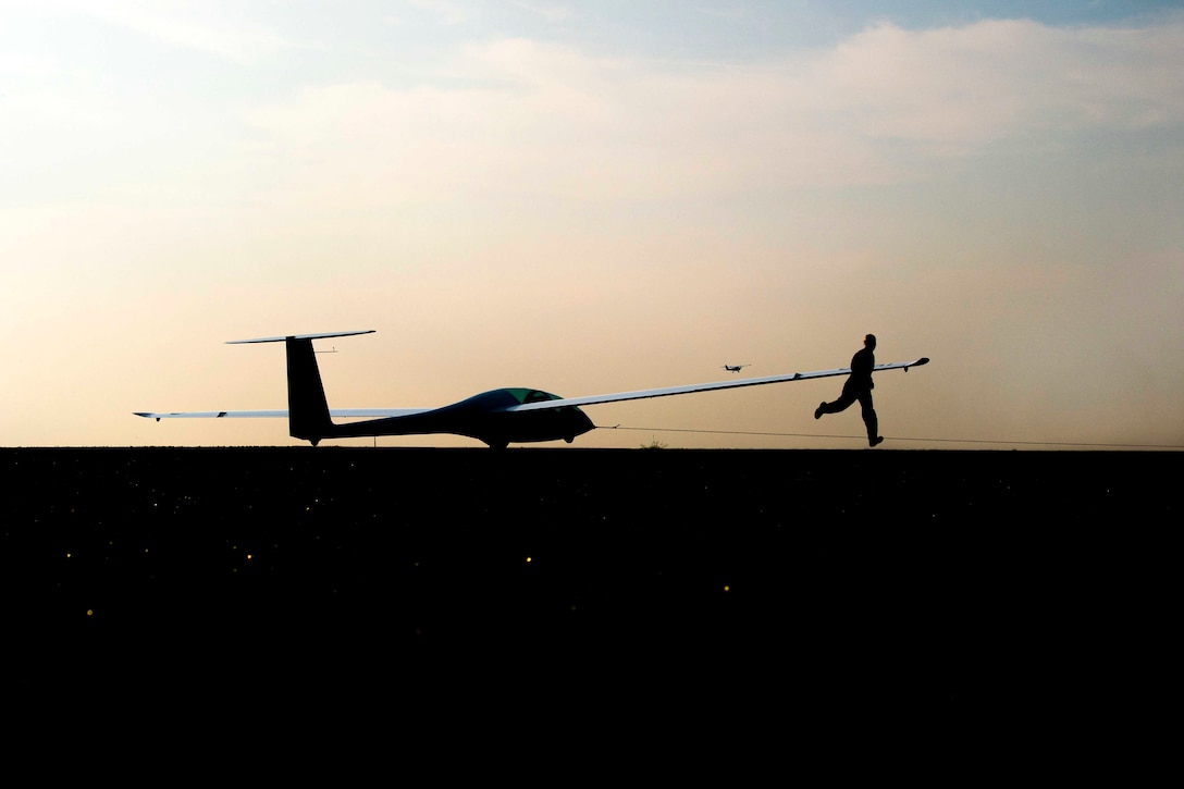 An Air Force cadet shown in silhouette runs next to an unmanned aircraft.