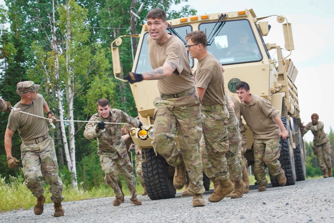 Airmen pull and push a tactical vehicle along an unpaved road.
