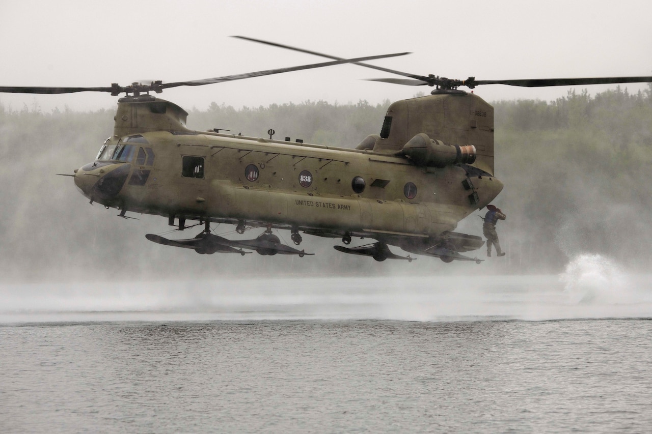 A soldier jumps from a helicopter into a body of water.