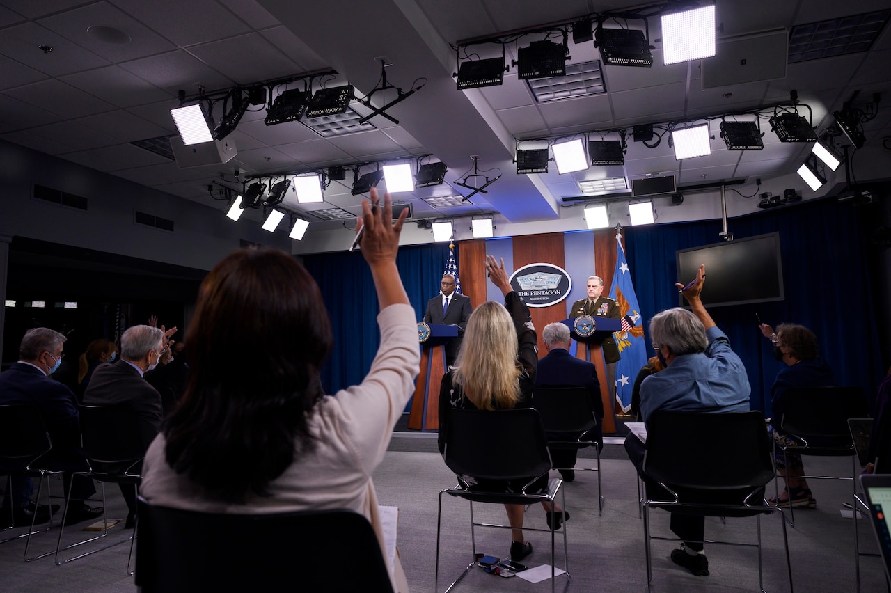 Secretary of Defense Lloyd J. Austin III and Joint Chiefs Chairman Army Gen. Mark A. Milley stand at a podium while reporters raise hands.