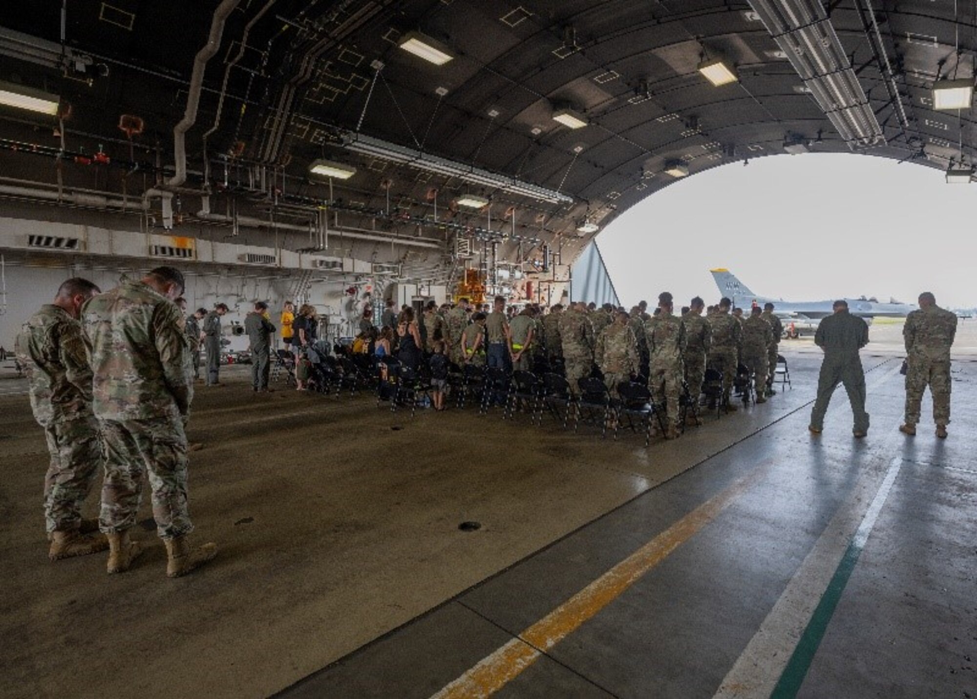 Airmen and families listening to an invocation during a ceremony in a hanger.