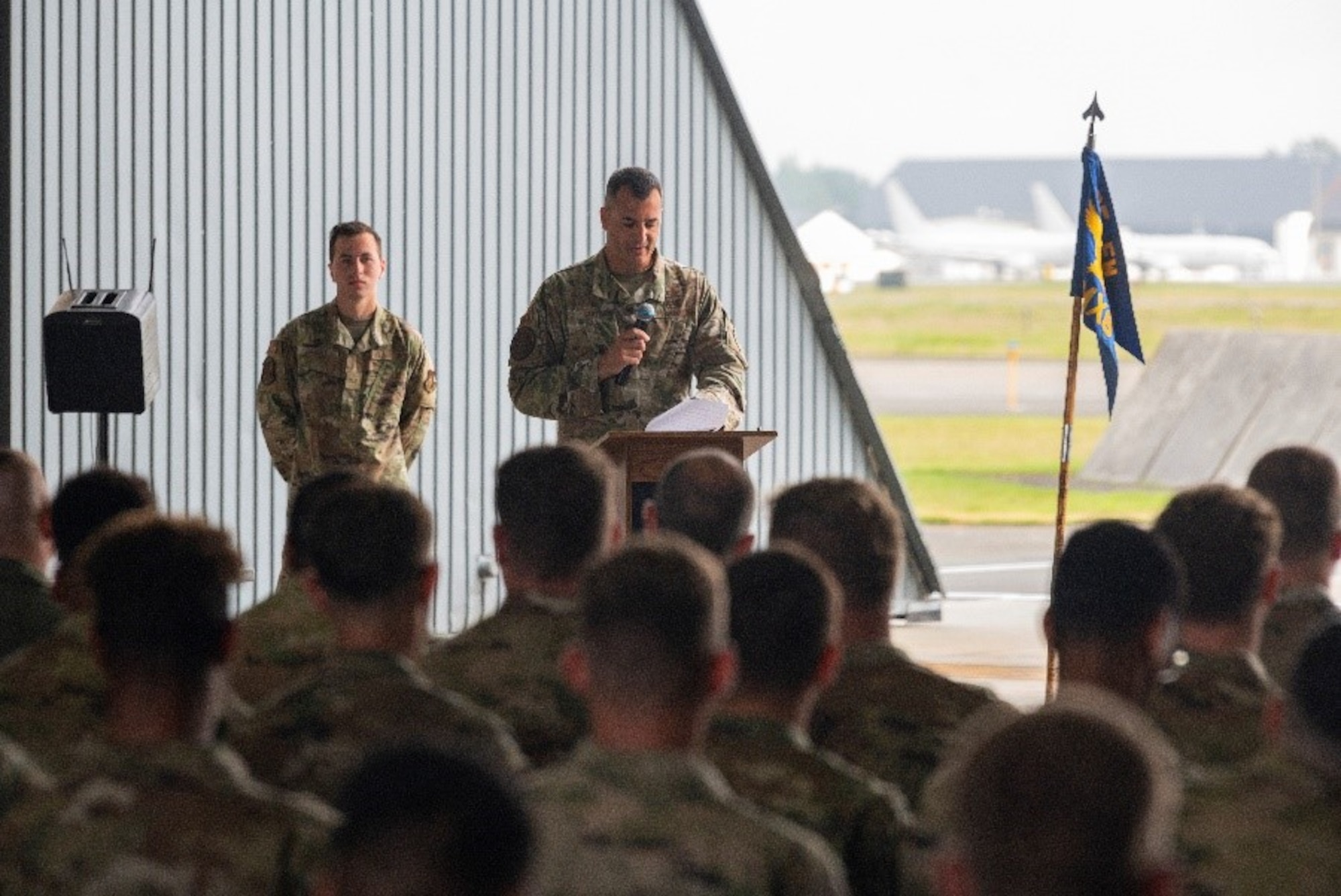Military member address a hangar full of people during a ceremony.