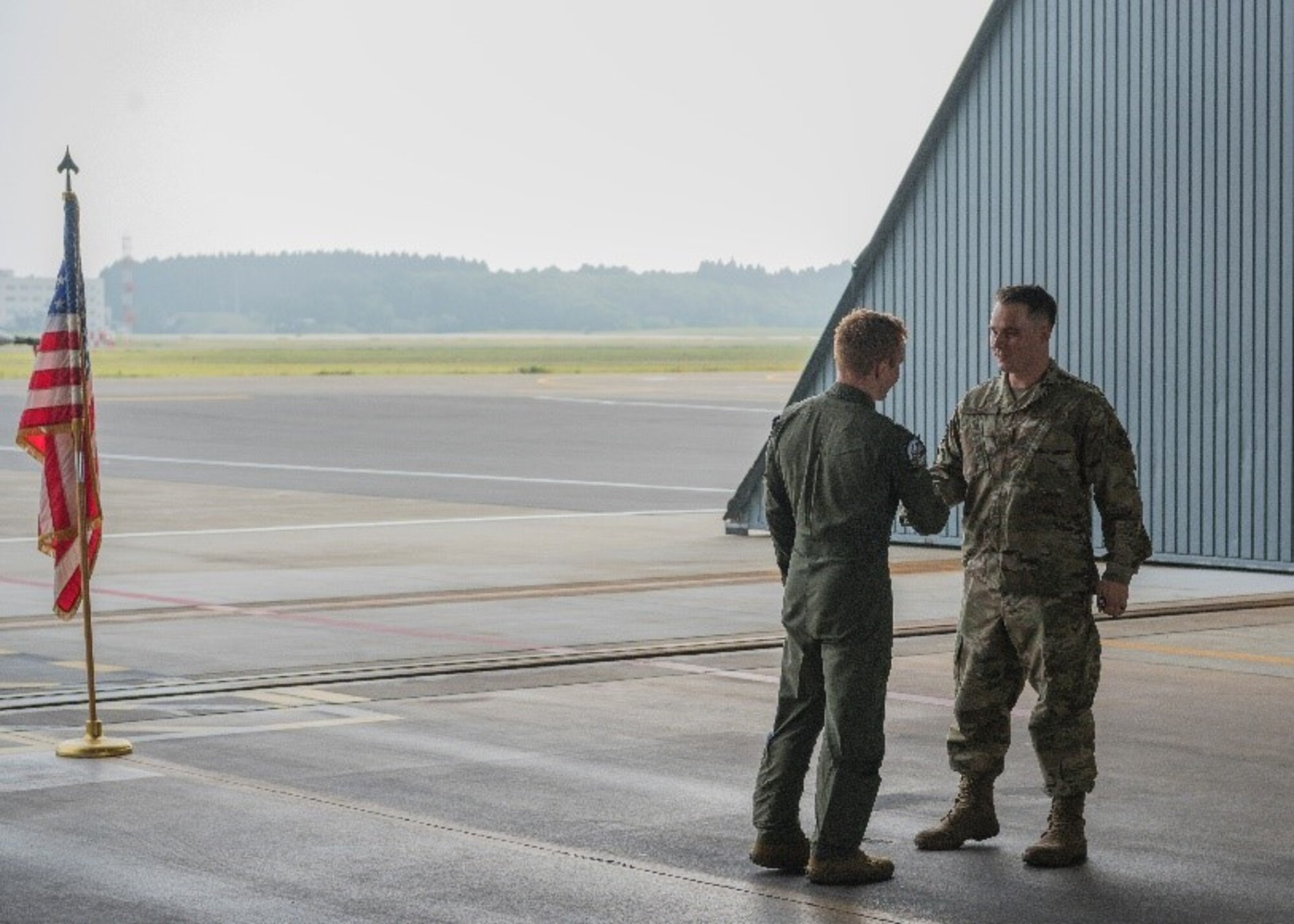 Military member gives another military member a coin and a handshake.