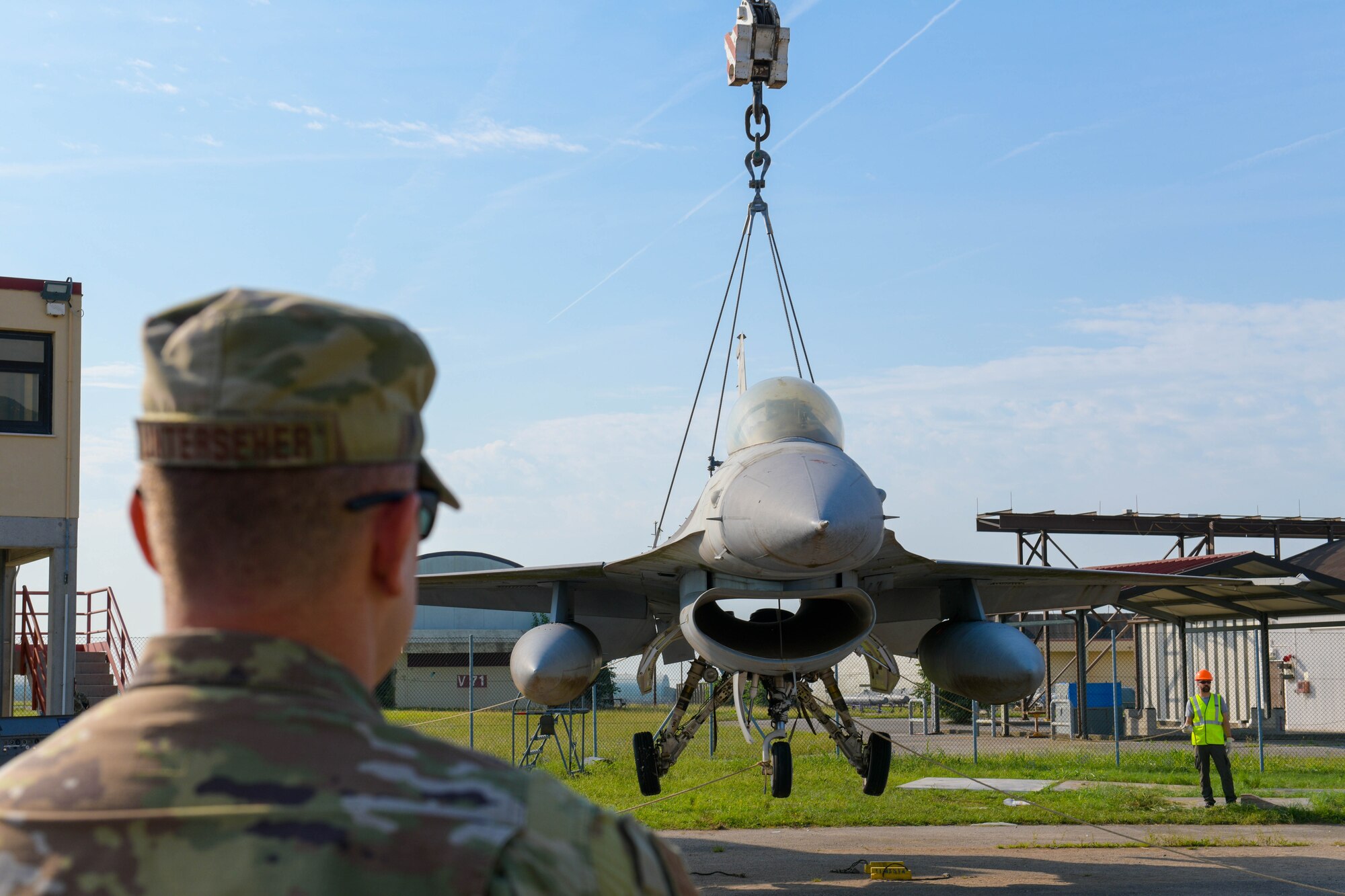 Chief Master Sgt. Jeremy Unterseher, 31st Fighter Wing command chief, watches as a U.S. Air Force F-16 Fighting Falcon is lifted off the ground during an annual Crash, Damaged or Disabled Aircraft Recovery (CDDAR) lift certification at Aviano Air Base, Italy, Aug. 13, 2021. The 31st FW and 52nd FW, Spangdahlem Air Base, Germany, participated in CDDAR training to recertify on the correct procedures of lifting an aircraft during an emergency. The purpose of CDDAR training is to enhance readiness and stay current on qualifications. (U.S. Air Force photo by Senior Airman Brooke Moeder)