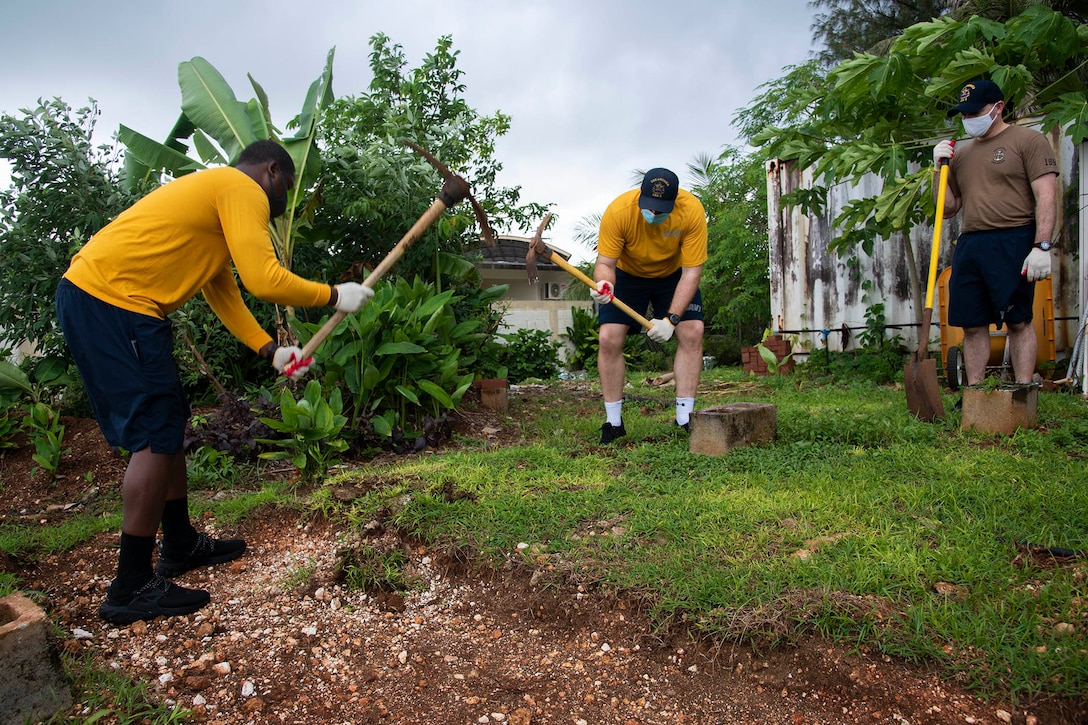 Three sailors use picks and shovels to create a garden.
