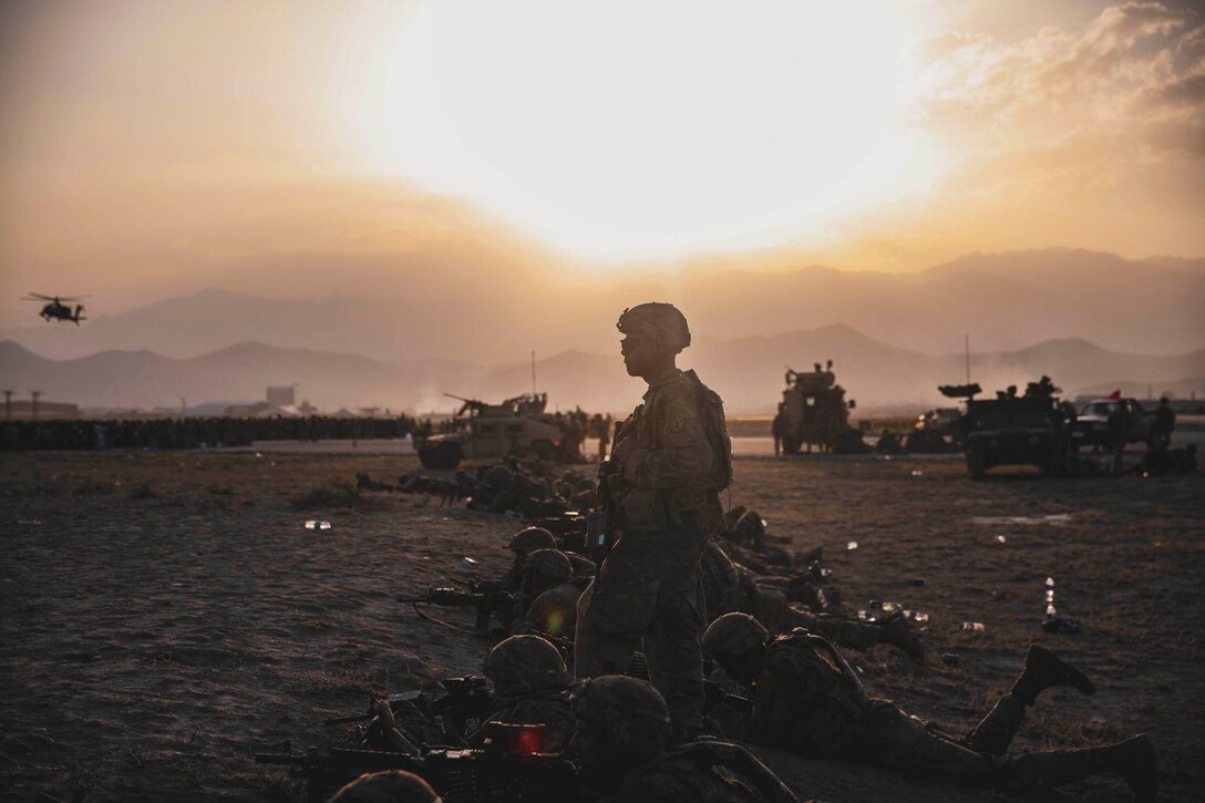 A row of soldiers lie on the ground with weapons at twilight.