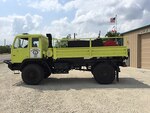 A former military truck sits in front of a fire department painted in fire truck yellow.